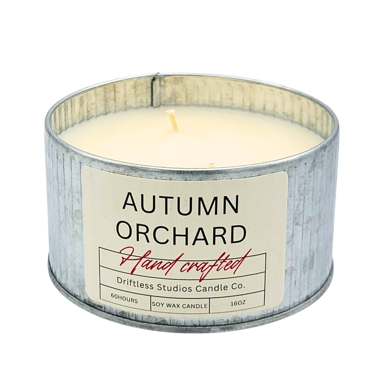 An 16oz soy wax candle in a galvanized metal tin with a cream-colored label that reads 'AUTUMN ORCHARD' and 'Hand crafted' by Driftless Studios Candle Co.