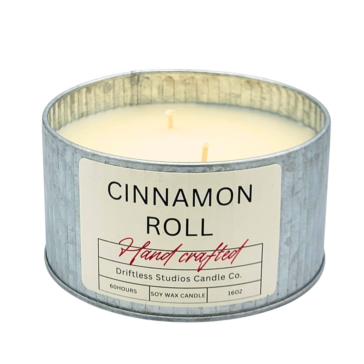 A round galvanized metal tin candle with cream-colored soy wax and two wicks, featuring a white label that reads 'CINNAMON ROLL' and 'Driftless Studios Candle Co.' on a plain white background.