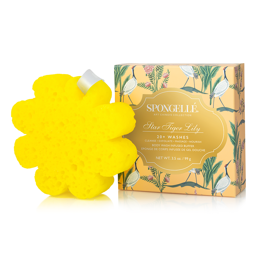 A yellow flower-shaped sponge from Spongellé next to its illustrated product box, featuring a gold label and botanical crane artwork on a white background.