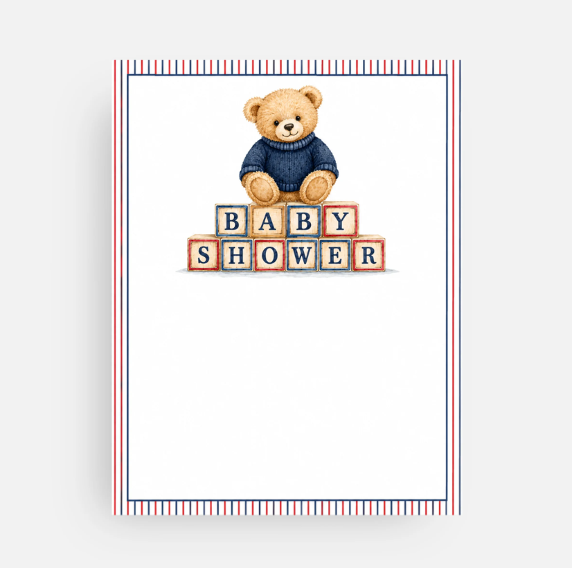 A baby shower card featuring an illustration of a teddy bear in a navy blue sweater sitting on toy blocks that spell 'BABY SHOWER'. The card has a white center, a red, white, and blue striped border, and is shown against a light gray background.