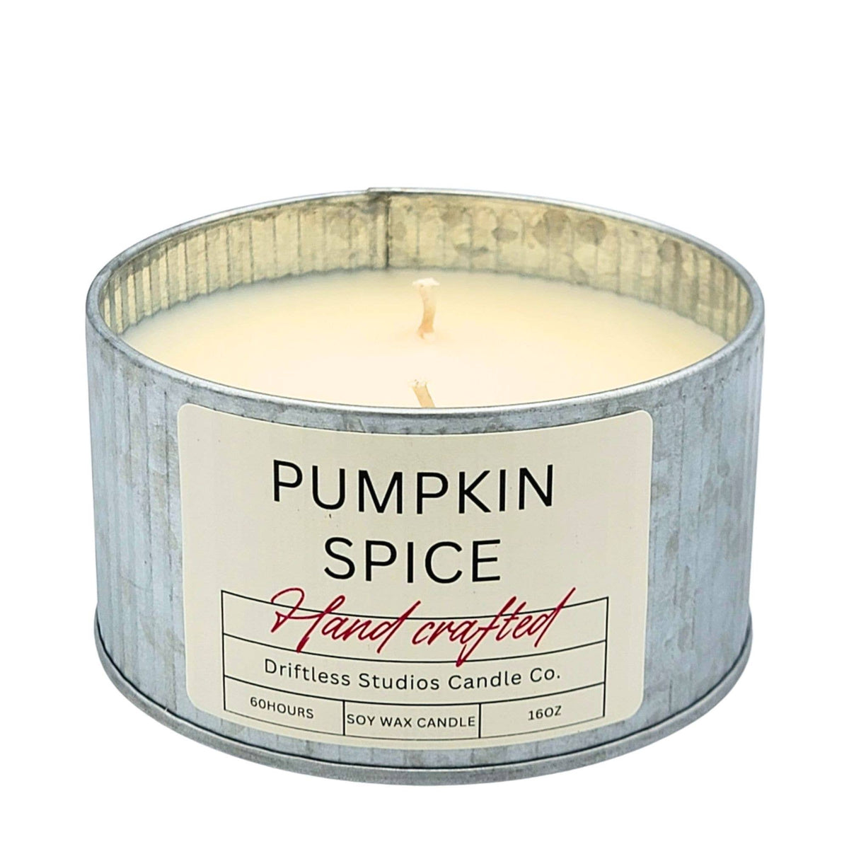A single-wick soy wax candle in a galvanized metal tin with a cream-colored label that reads 'PUMPKIN SPICE' and 'Hand crafted' by Driftless Studios Candle Co.